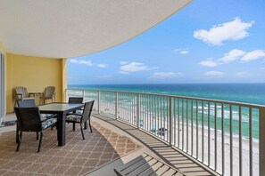Un balcon avec une table et des chaises, donnant sur une plage, l’océan et un ciel dégagé.