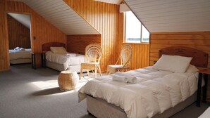 Una camera da letto accogliente, con arredamento in legno, due letti, poltrone in vimini e un'ampia finestra che lascia entrare la luce naturale.