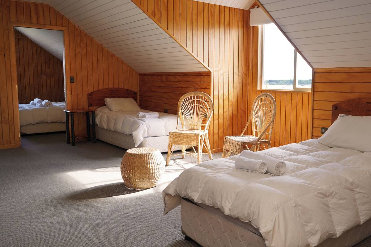 Ett mysigt sovrum med trätema, utrustat med två sängar, flätade stolar och ett stort fönster som sl äpper in naturligt ljus.