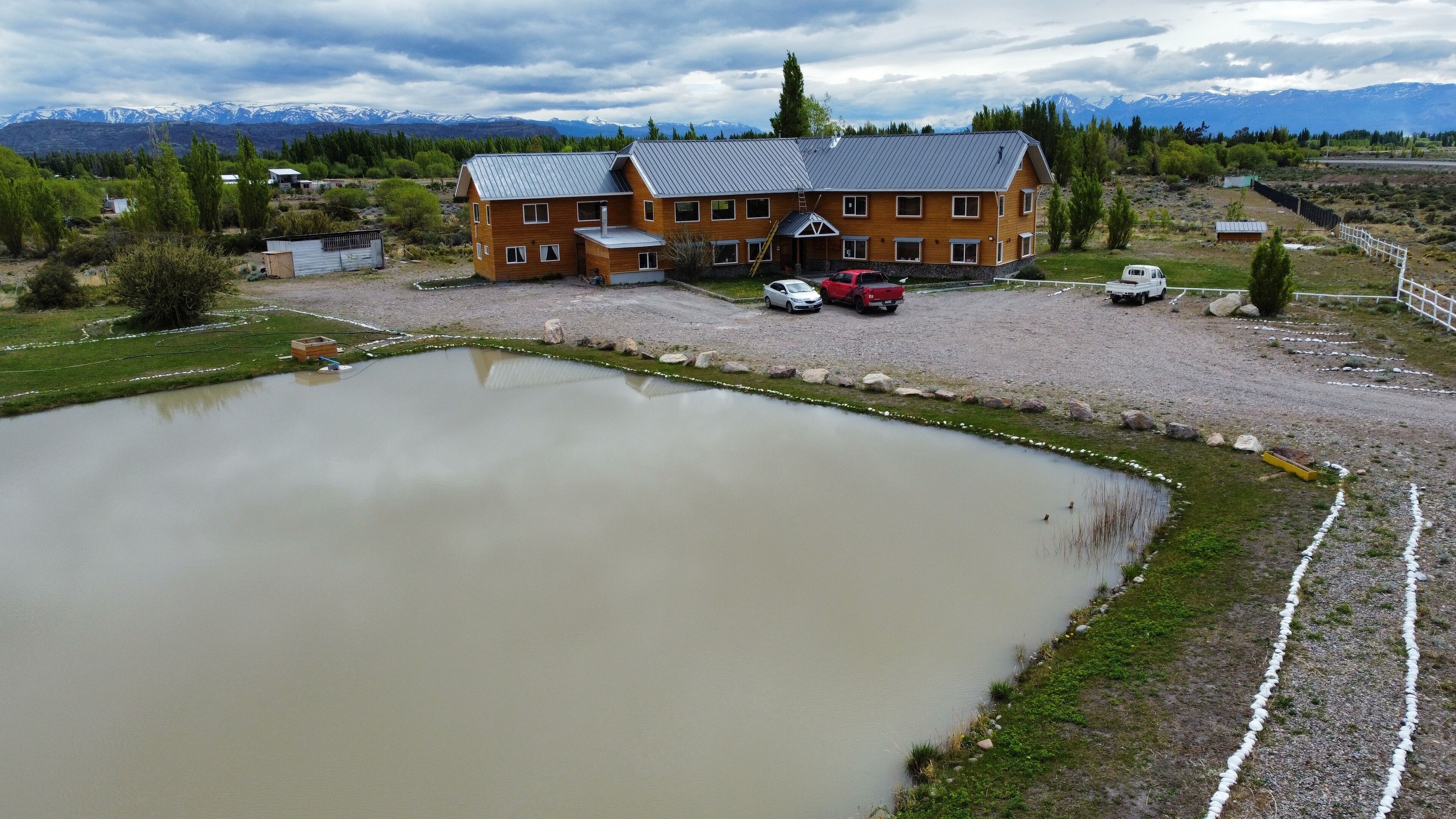 A large building with a sloped roof, a pond, and a mountainous backdrop.