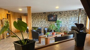 Una hall moderna di un hotel con parete in pietra, elementi in legno e televisore a schermo piatto fissato al muro.