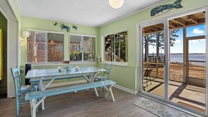 Een eetgedeelte met een glazen tafel en banken, grote ramen met zonwering en uitzicht op het strand door een schuifdeur.