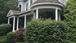 A large, two-story house with a wrap-around porch, a turret, and a chimney.