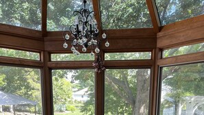 A round glass table with six chairs in a sunroom with large windows.