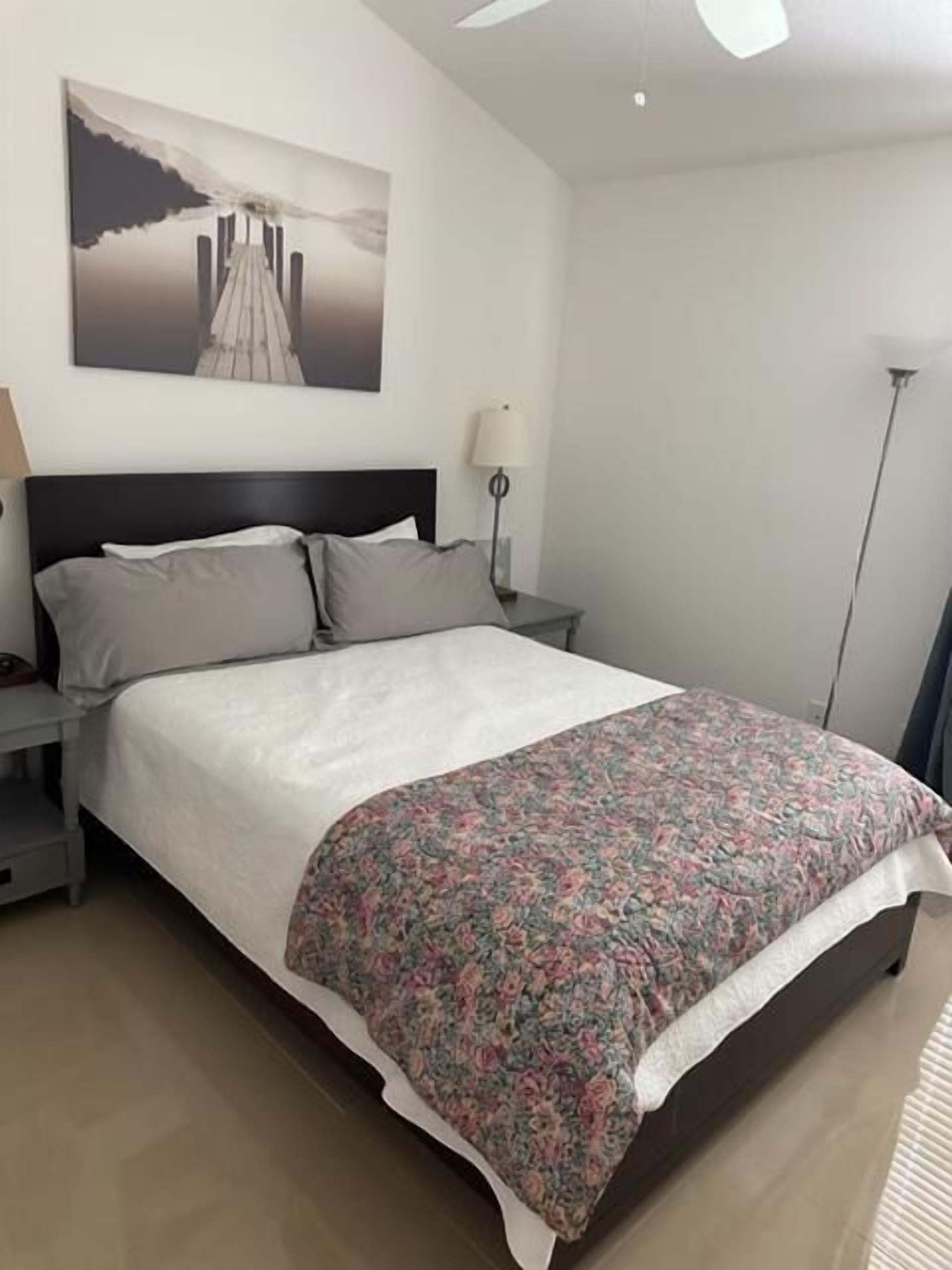 Una camera da letto con un letto grande, un comodino, una lampada e una ventola a soffitto.