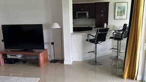 Una sala de estar moderna con un televisor de pantalla plana, un sofá y una zona de comedor con taburetes de bar.