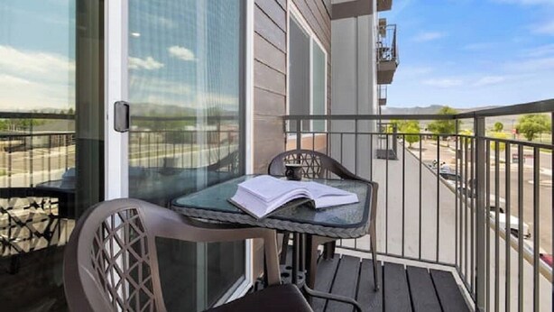 Een balkon met een glazen deur, een klein tafeltje met een boek en een stoel.
