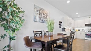 Een moderne eetruimte met een houten tafel en stoelen, een potplant en een stadsgezichtschilderij aan de muur.