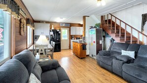A spacious living area with a sofa, a dining table with chairs, a kitchen with wooden cabinets, and a staircase leading to another level. - Kineo Point (Waterfront on Moosehead Lake) (Rockwood)