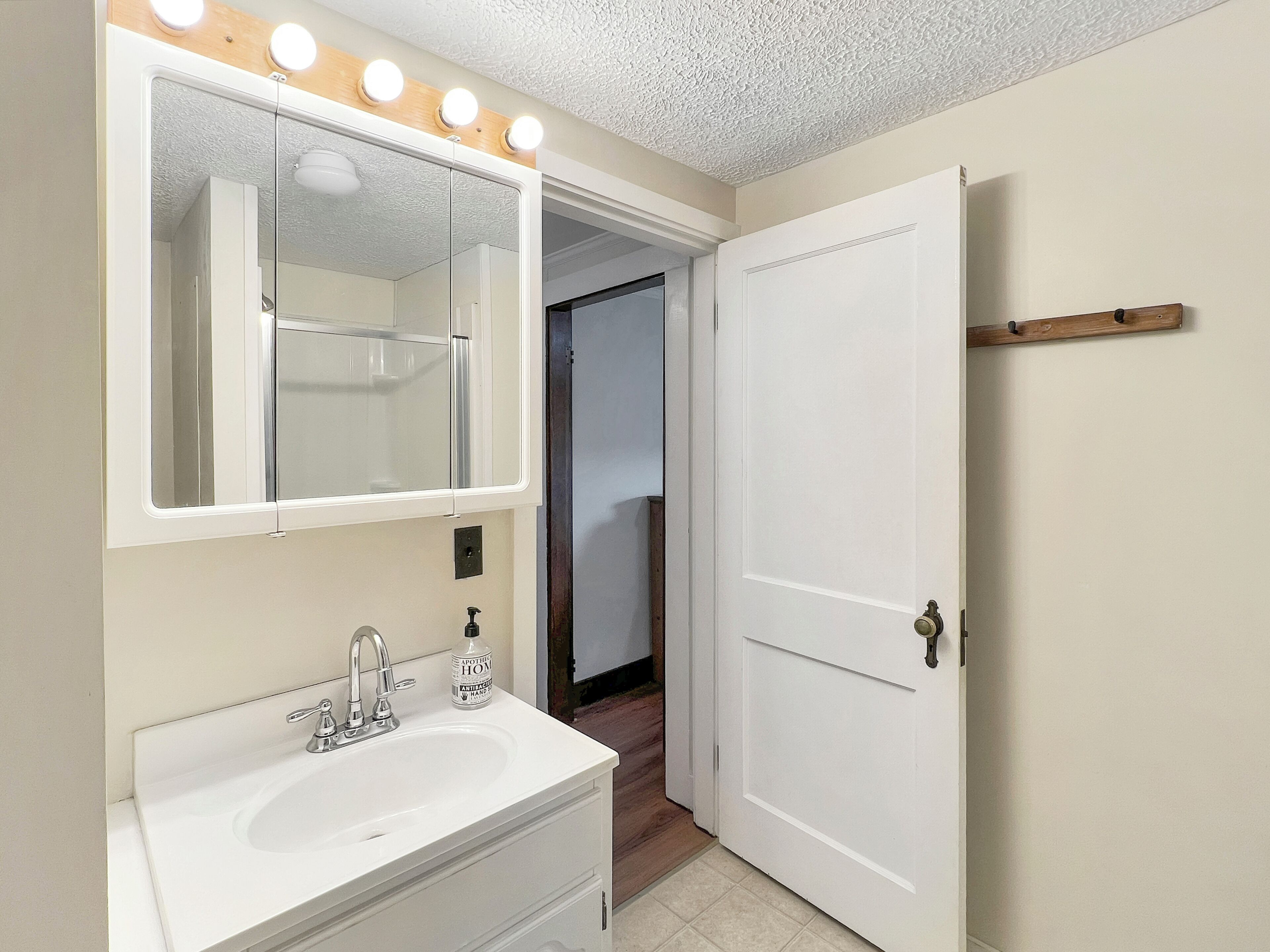 Un baño con un lavabo blanco, un espejo grande con iluminación y una puerta que da a otra habitación.