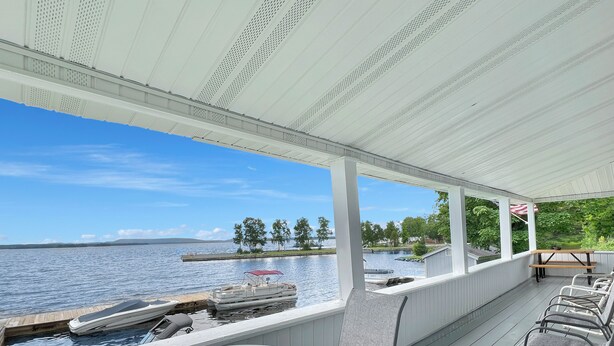 A covered outdoor area with a view of a lake, a dock with boats, and a picnic table with chairs. - Kineo Point (Waterfront on Moosehead Lake) (Rockwood)