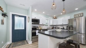A modern kitchen with white cabinets, stainless steel appliances, and a central island with stools. - Channel Charmer - Prime Gun Lake Waterfront Stay (Shelbyville)