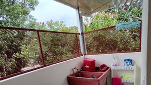 A small balcony with a red sink, a blue laundry basket, and a white shelf with cleaning supplies.