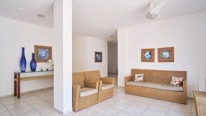 A spacious living area with two wicker sofas, a glass coffee table, and framed artwork on the walls.