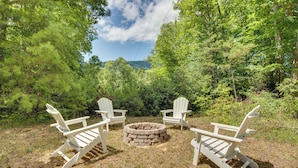 A circular stone fire pit surrounded by four Adirondack chairs in a forested area. - Secluded Mountain Retreat: 30 Mi to Asheville! (Old Fort)