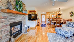 A living room with a fireplace, a TV mounted on the wall, a dining area with wooden furniture, and a ceiling fan. - Peace at Echota - Direct Grandfather Mtn Views! (Banner Elk)