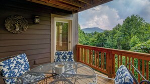 A wooden deck with a round table and chairs, a door, and a view of a forested mountain range. - Peace at Echota - Direct Grandfather Mtn Views! (Banner Elk)