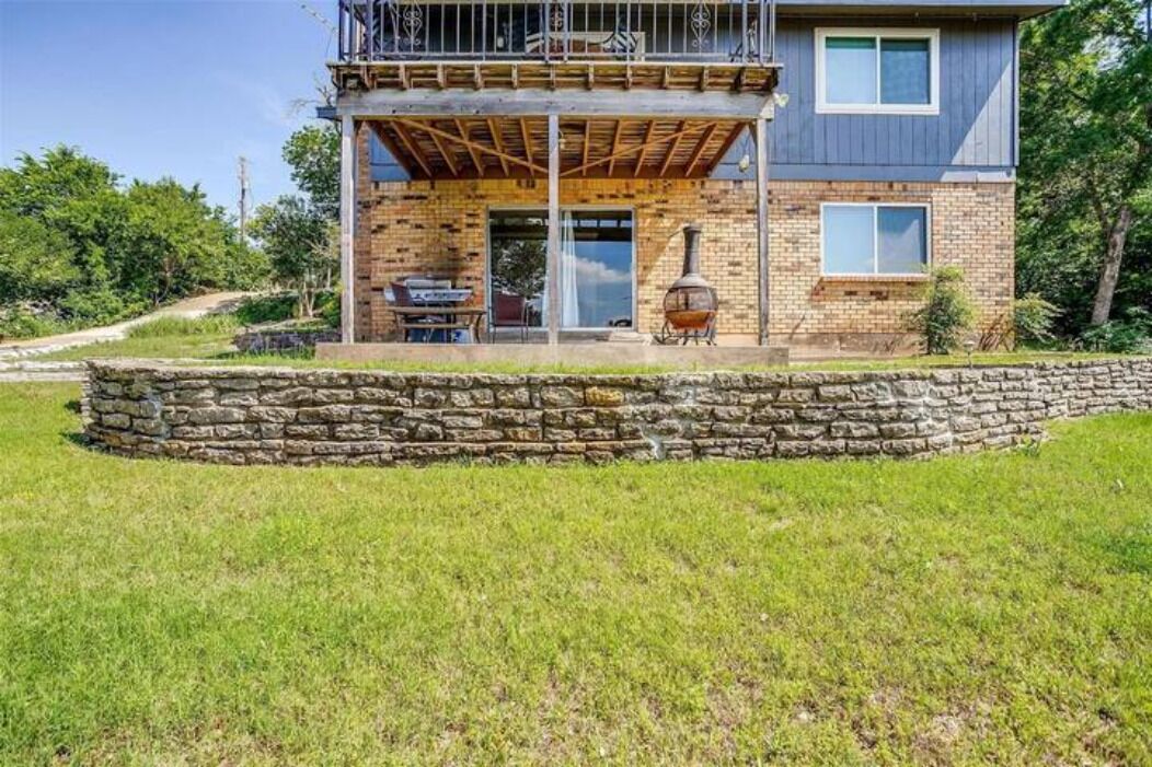 A two-story house with a stone foundation, a wooden deck, and a chimney.