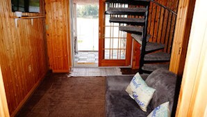 Un intérieur en bois avec un canapé, un escalier et une porte donnant sur l’extérieur.