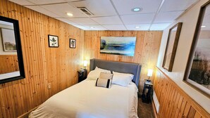 Une chambre d’hôtel avec un grand lit, des murs recouverts de panneaux de bois, un tableau au-dessus du lit et une fenêtre sur le côté droit.