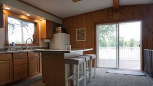 Une cuisine avec des meubles en bois, un îlot central doté de tabourets, une grande fenêtre et une porte-fenêtre coulissante donnant sur un espace extérieur.