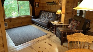 A cozy cabin interior with a sofa, a chair, a lamp, and a fireplace.