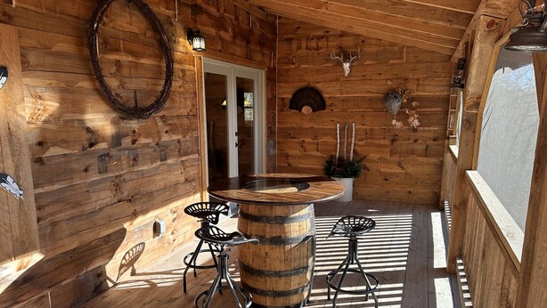 A wooden cabin interior with a bar area featuring two stools, a wooden barrel, and a decorative skull on the wall.