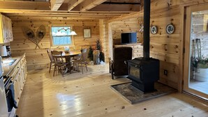 A cozy cabin interior with a dining area, wooden walls, a fireplace, and a television.