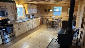 A wooden cabin interior with a kitchen, dining area, and a wood stove.
