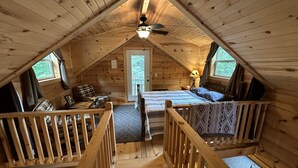 A cozy attic bedroom with a bed, a chair, a small table, and a window.