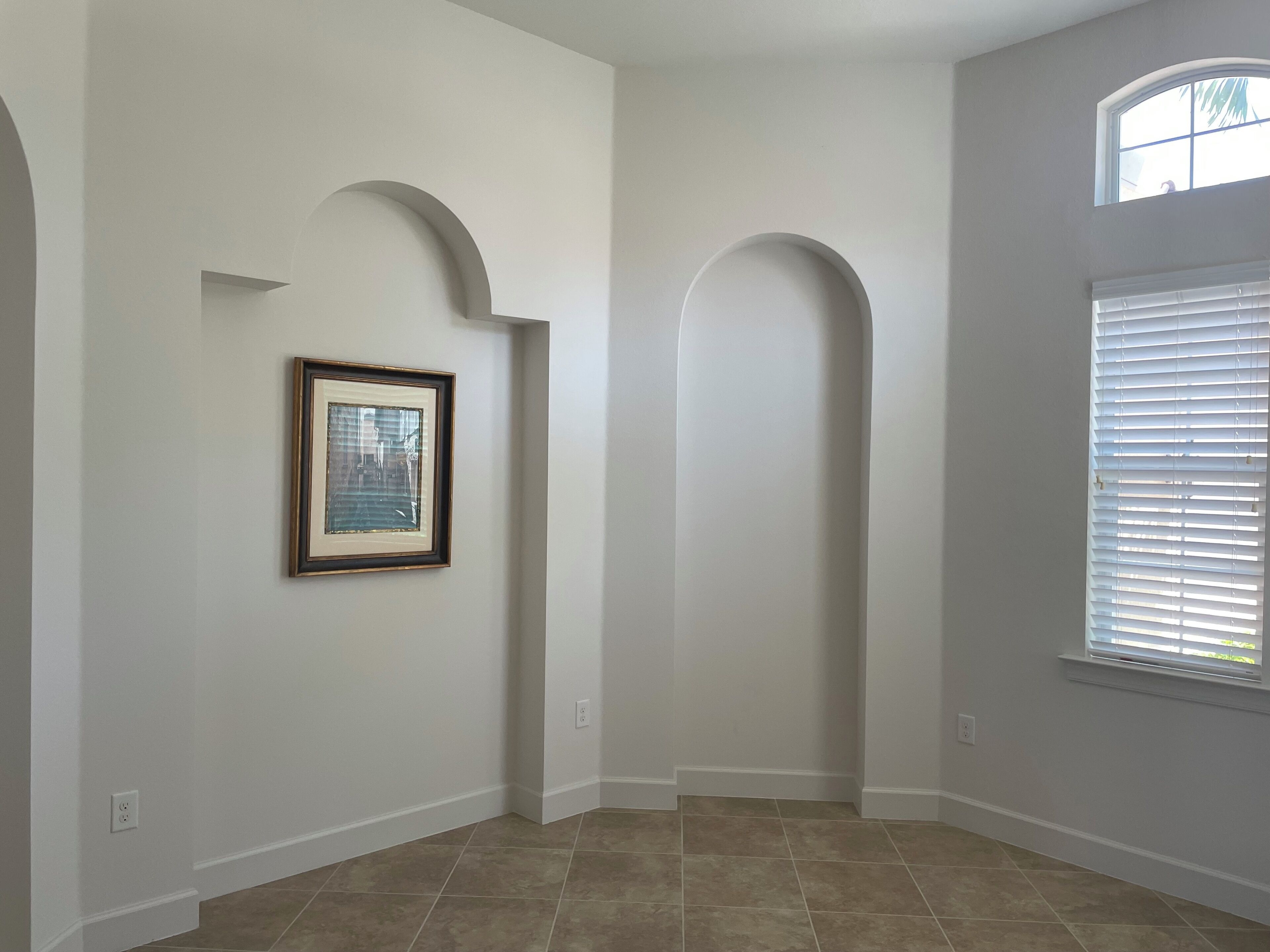 A spacious hallway with white walls, a framed picture, and a large window with blinds.