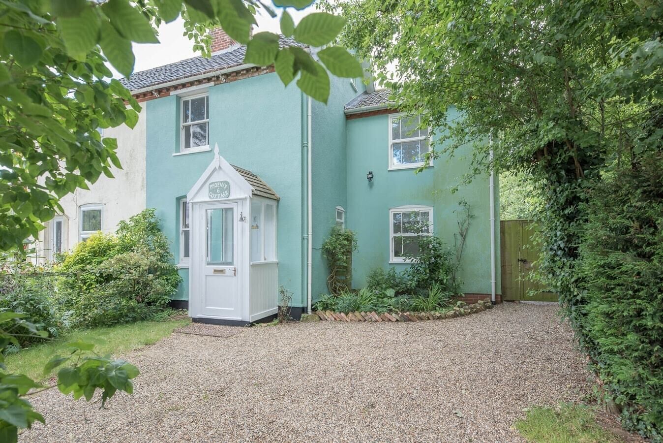 A cottage with a gravel driveway, a small white door, and a sign reading "Phoenix Cottage."