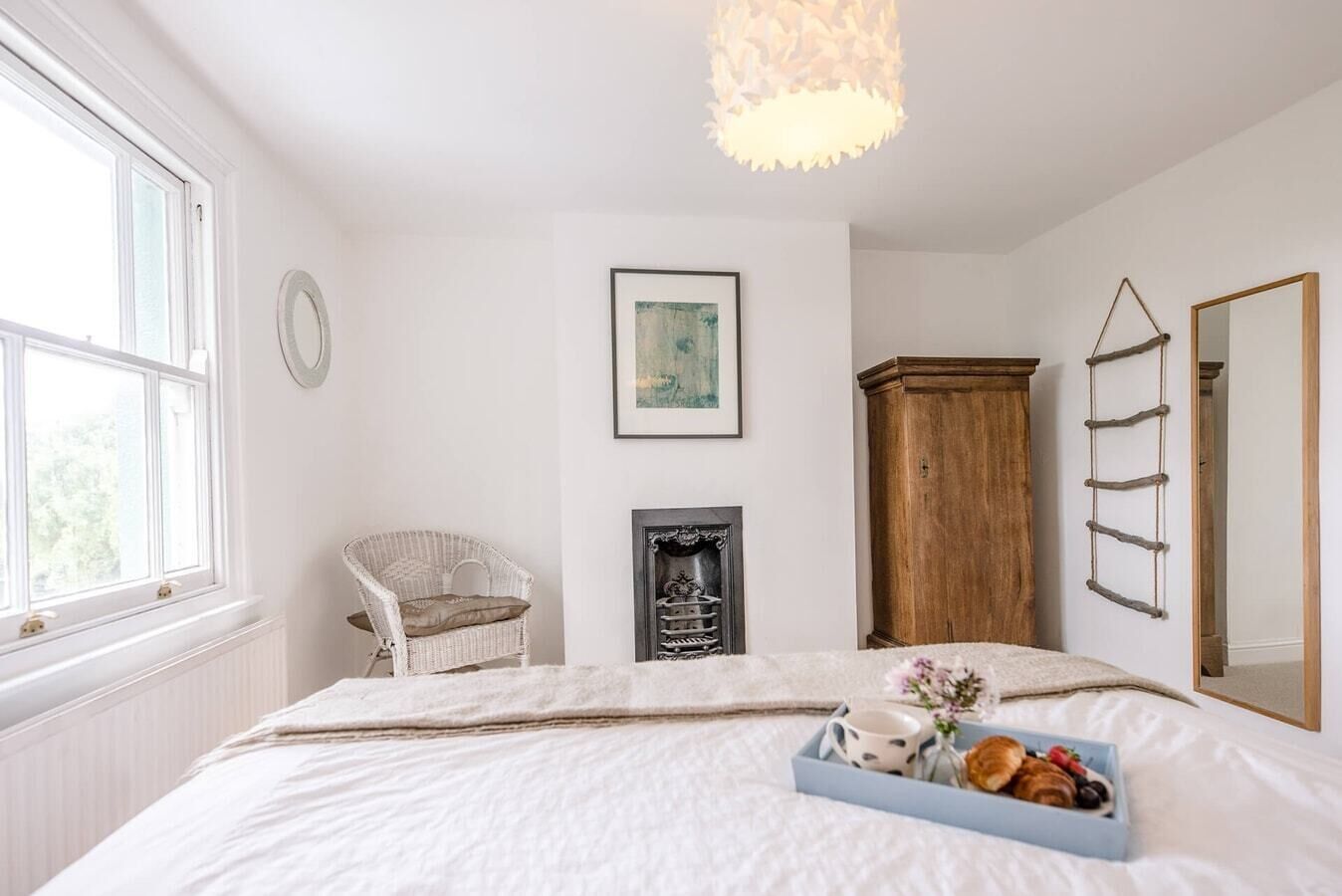 Ein Schlafzimmer mit Bett, Sessel, Kamin, Kleiderschrank, Spiegel und Fenster.