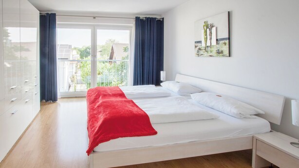 A modern bedroom with a large bed, a nightstand, and a view of the outdoors through a sliding glass door. - Traum-ferienwohnung Alpenblick, 75 qm, Balkon und Bergblick (Bad Aibling)