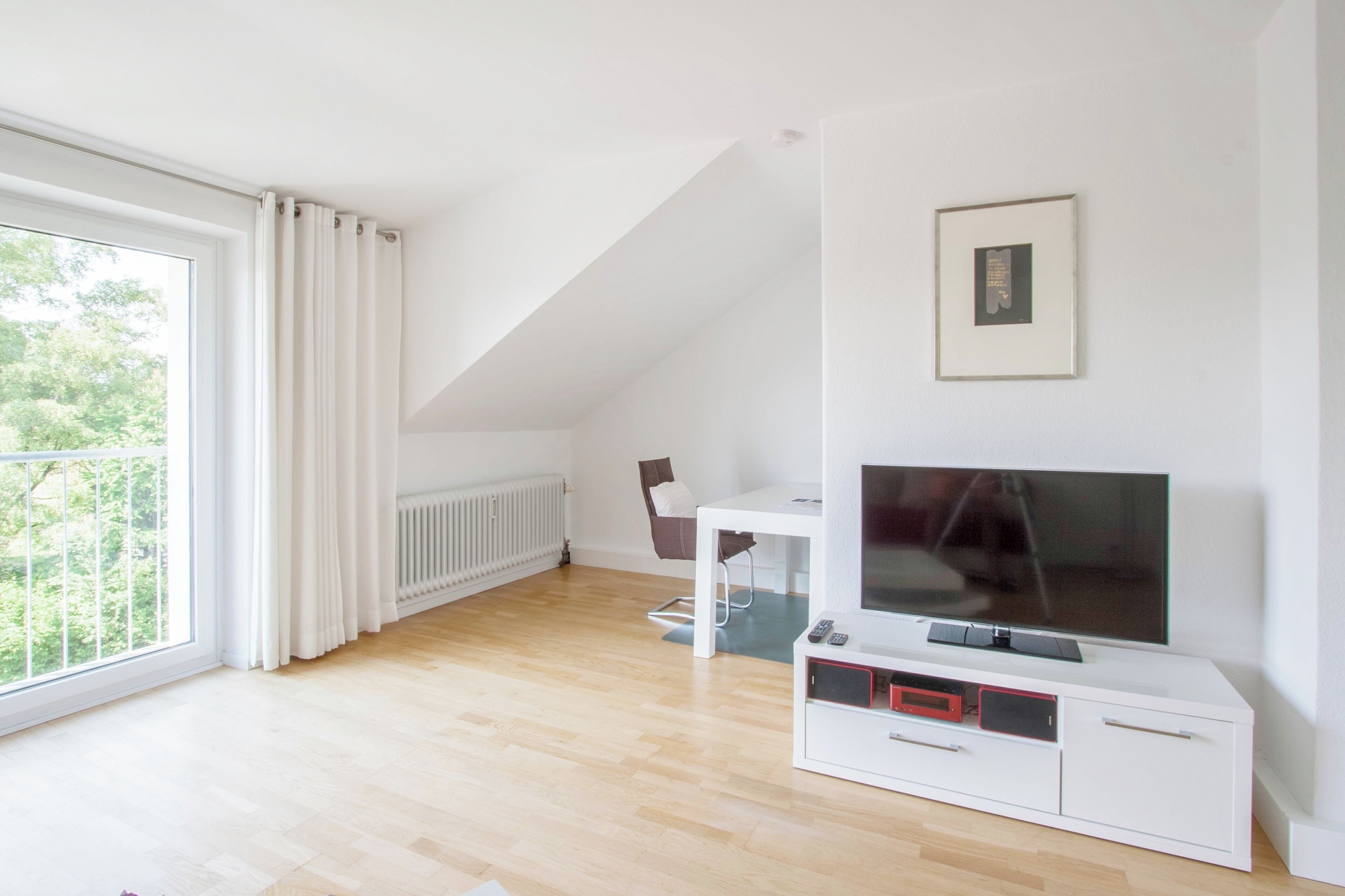 Een moderne woonkamer met een groot raam, een flatscreen televisie, een witte entertainmentkast en een fauteuil.