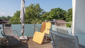 A deck with two lounge chairs, one grey and one yellow, and a white umbrella. - Traum-ferienwohnung Alpenblick, 75 qm, Balkon und Bergblick (Bad Aibling)