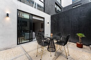 Eine moderne Außenpatio mit einem runden Tisch, Stühlen, einem Blumentopf und einer Glastür zu einem Innenbereich.