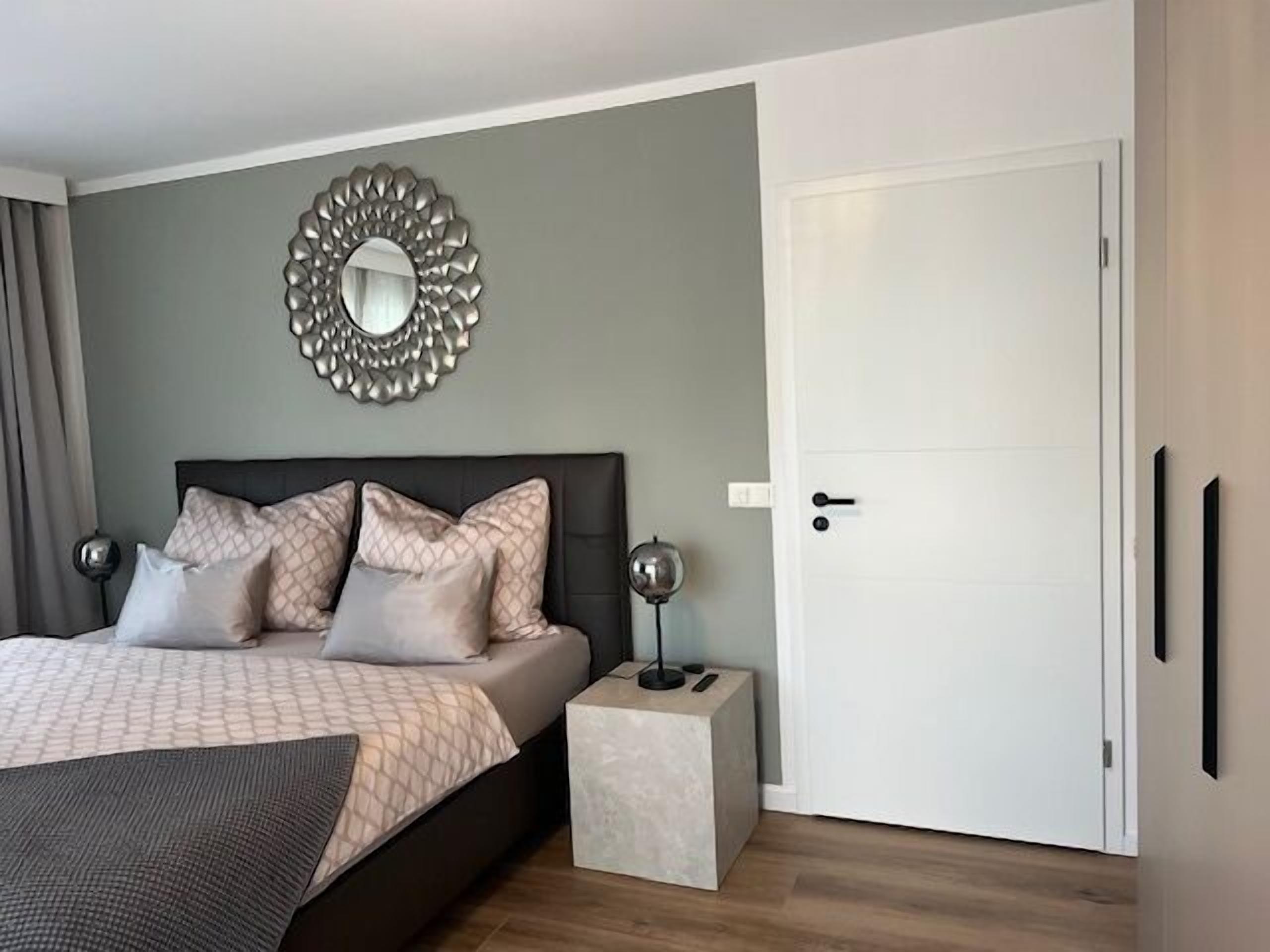 Quarto moderno com cama, mesas de cabeceira, espelho e porta.