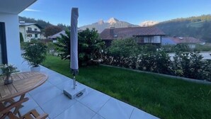 Un balcón con mesa y sillas, una planta en maceta y vistas a casas y montañas.