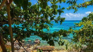 Een pad dat naar een strand leidt met helder turquoise water en rotsformaties.