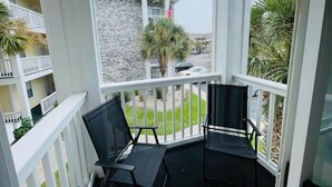 Een balkon met twee zwarte stoelen, een witte reling en uitzicht op een gebouw met een stenen gevel en een Amerikaanse vlag.