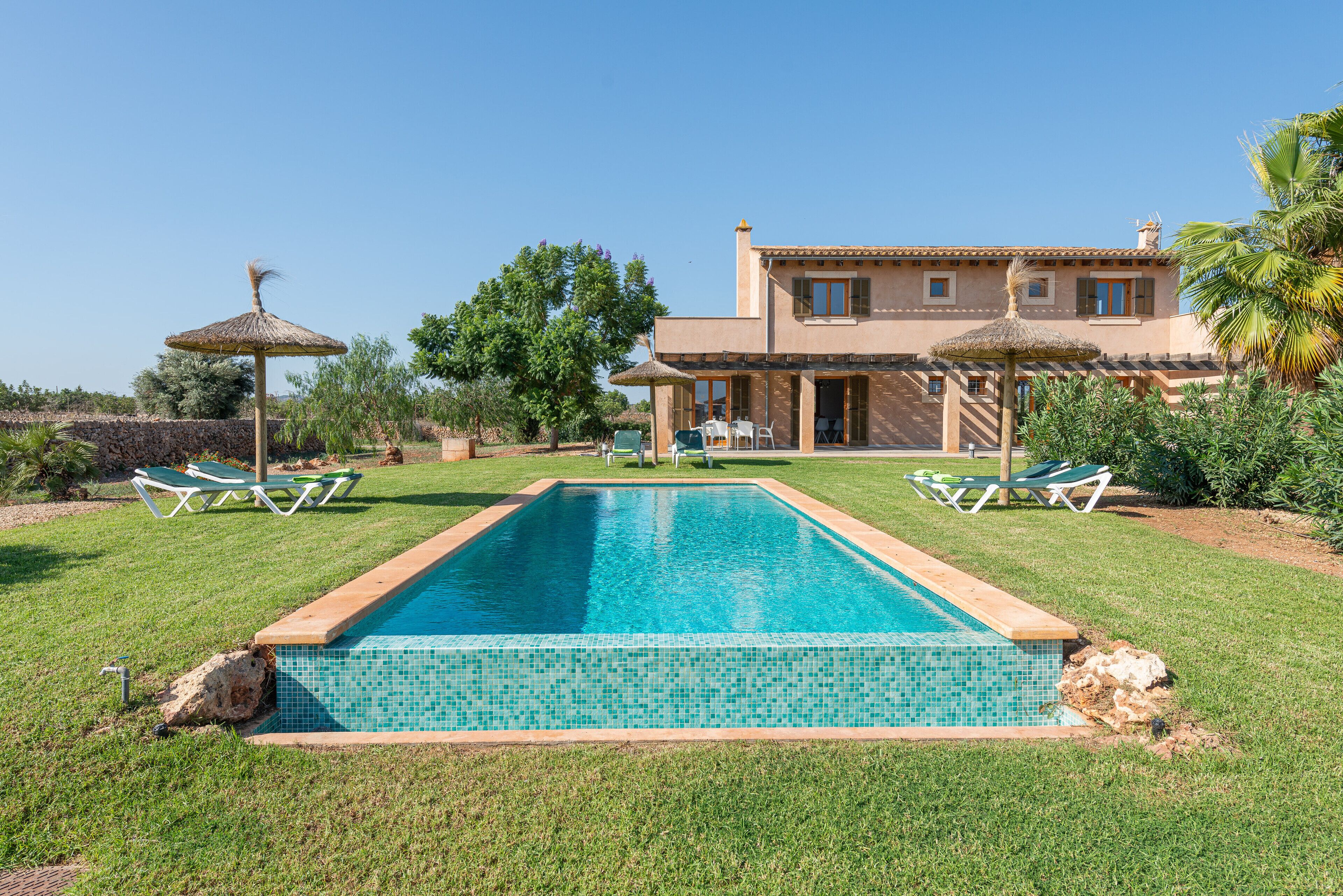 A swimming pool with a tiled edge, surrounded by grass and two lounge chairs.