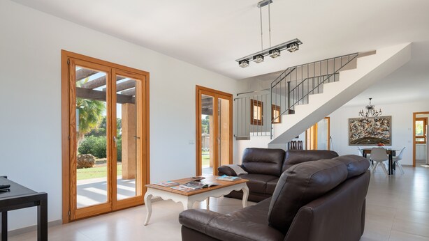 Un salon spacieux avec un canapé en cuir marron, une table basse en bois et un escalier menant à l’étage supérieur.