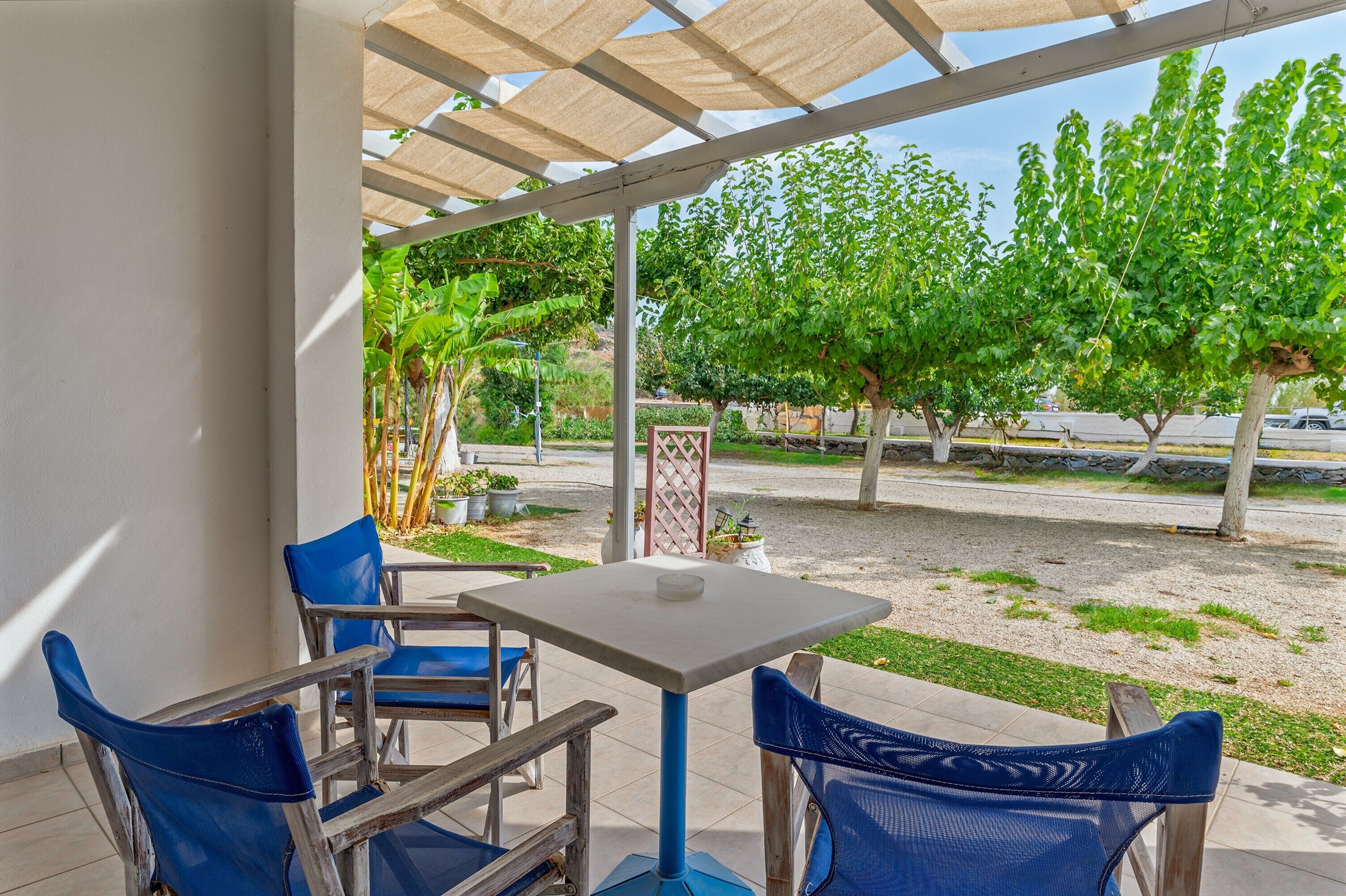 An outdoor patio with a table and chairs, a pergola, and a view of trees and a road.