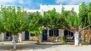 A building with a white exterior, blue shutters, and a covered outdoor seating area with tables and chairs. - Holiday Home '9 Perasma Kypri Beach' with Private Terrace, Wi-Fi and Air Conditioning (Kypri)