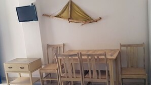 Una stanza con un tavolo e sedie in legno, un comodino con cassetti, una TV a muro e una struttura decorativa appesa.