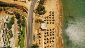 Vista aerea di una zona costiera con una strada, auto parcheggiate e una spiaggia con lettini.