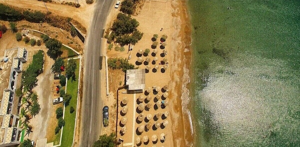 An aerial view of a coastal area with a road, parked cars, and a beach with sun loungers.