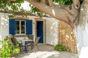 A patio with a table and chairs, a blue door, and a tree.