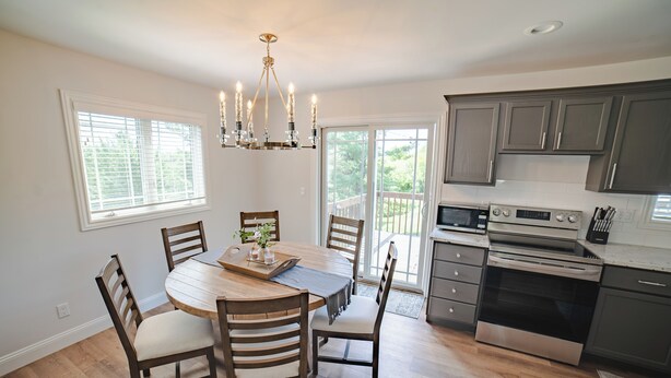 A modern kitchen with a dining area, featuring a wooden table, chairs, a chandelier, and stainless steel appliances.